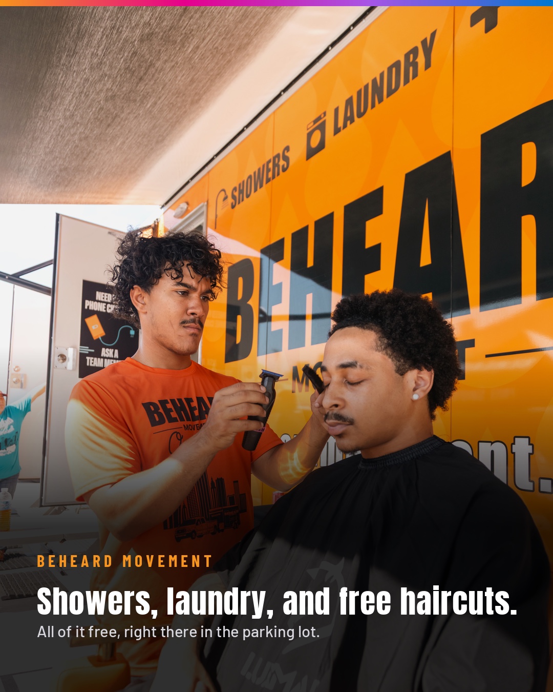 A BeHeard Movement team member giving a free haircut beside the mobile shower and laundry trailer.